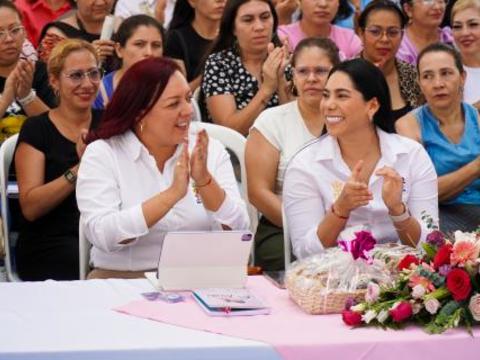 Mujeres en primera fila del evento aplauden y sonríen con entusiasmo, sentadas en una mesa decorada con flores y materiales del programa.